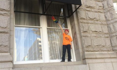 BCC student Marxe Orbach climbs onto a Trump Hotel window and waves a rainbow flag, as a crowd of protesters watches. Photo by Yael Hanadari-Levy.