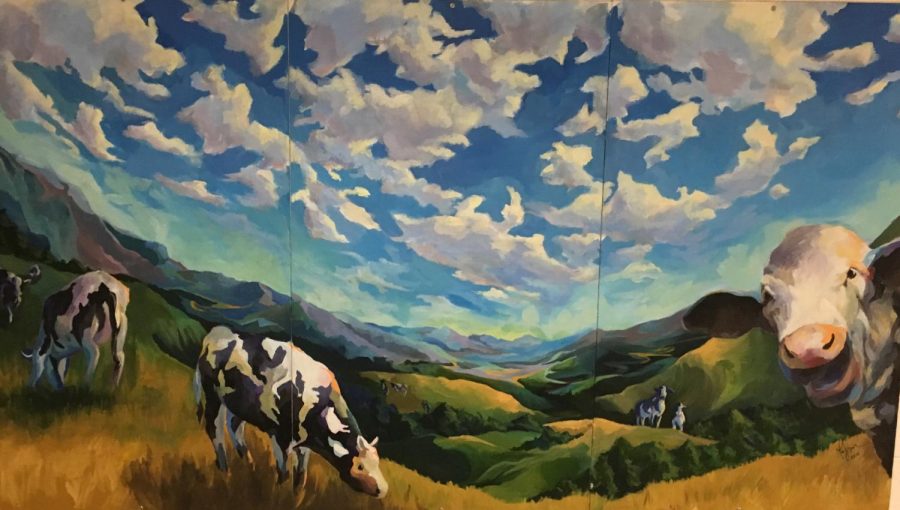 This mural of cows grazing in a field is hangs near the gym on the main level of the school. This piece of art is one of the many that students question the origin. Photo by Jessica Silverman