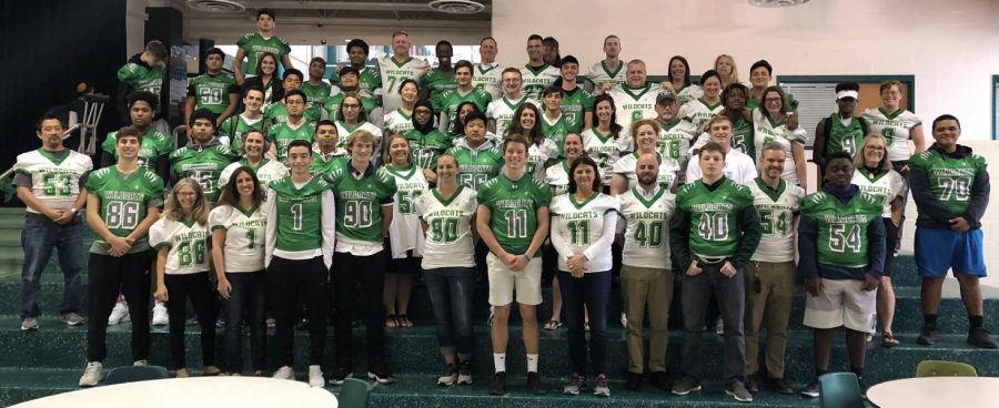 The football team stands alongside their mentors wearing their jerseys.