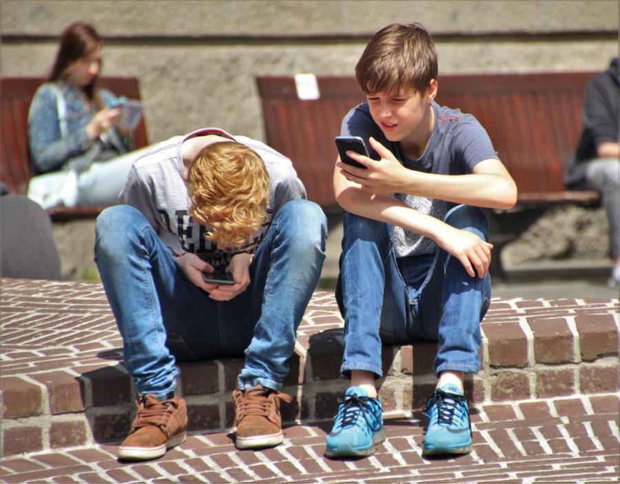 Two young boys sit adjacent to one another yet are not socializing. Given that the average age of cell phone users is so young nowadays, this sight is not a rarity.