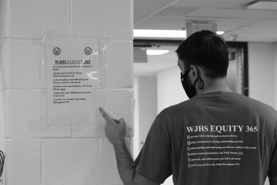 Counselor James Stradley wears his Equity 365 shirt and points to an Equity 365 sign. Signs were posted throughout hallways to remind students and staff to follow the initiatives steps.