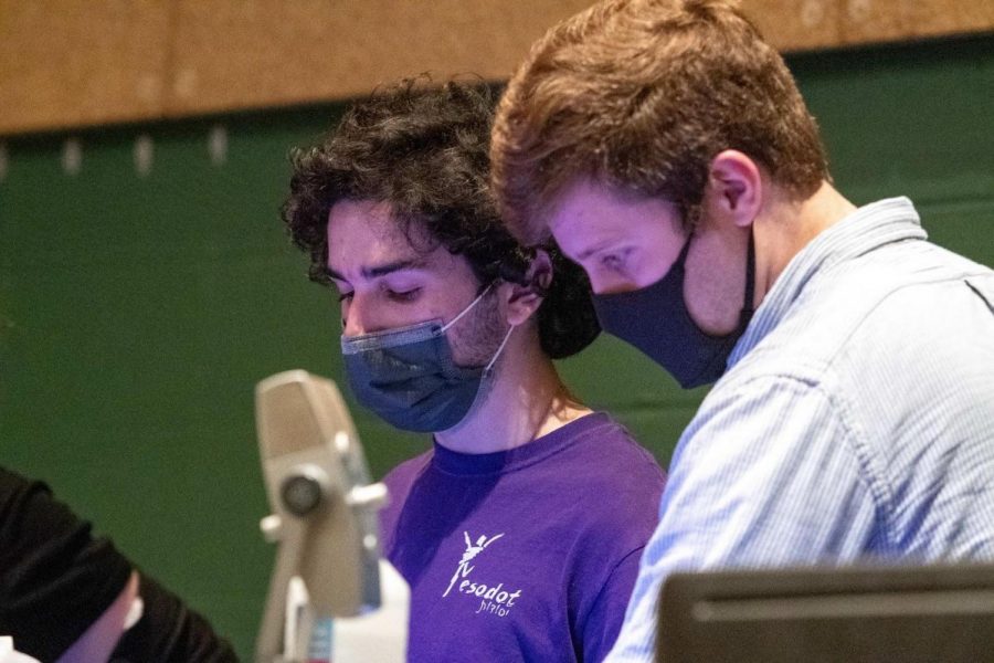 From left: audio master senior Noam Levy and Assistant Technical Director Matt Silverman check the workability of the microphones at the soundboard in the back of the auditorium during a crew meeting. “A lot of our preparation is teaching the people in audio how to mic, making sure all of our equipment is working well and organizing everything to get ready to mic and do audio,” Levy said.