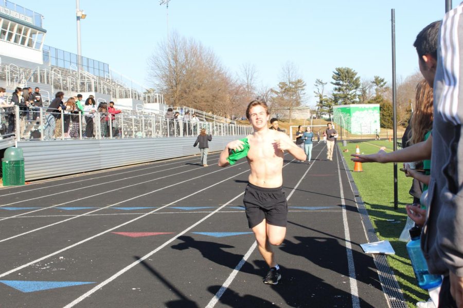 Junior Matt Uhl taking his t-shirt off before the finish line while being encouraged by the audience members on the side of the track. Not only were there many runners in the race, but a large audience came to support as well.