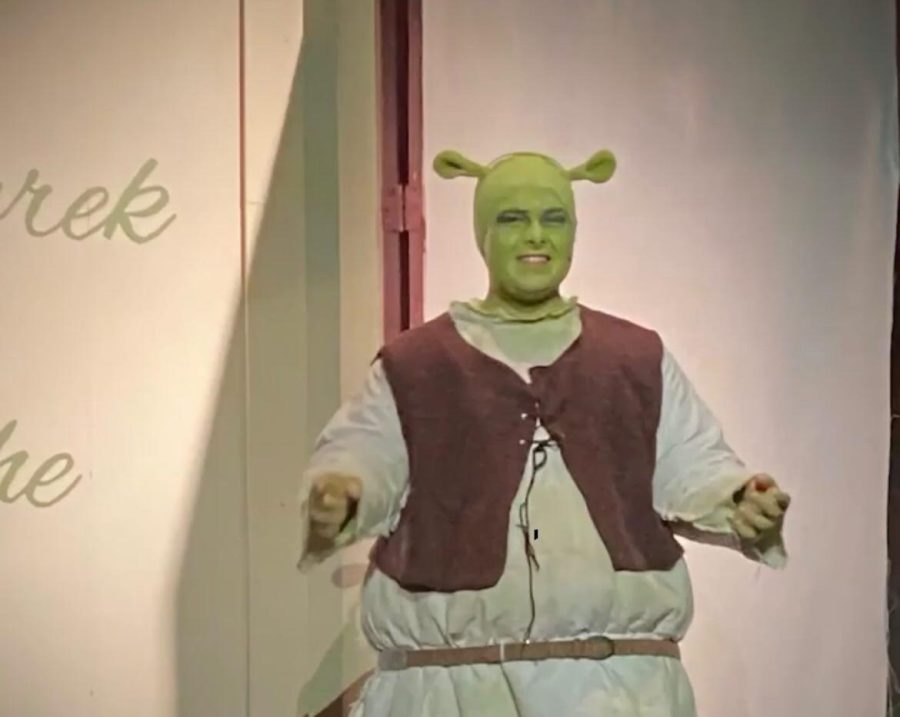 This photo (taken 35 feet away due to the repelling effects of his odor) shows Biggs in 6th period Madrigals just 2 days before the opening of Shrek. His intense methods such as  not showering and dressing as Shrek out of rehearsals have been polarizing among students.