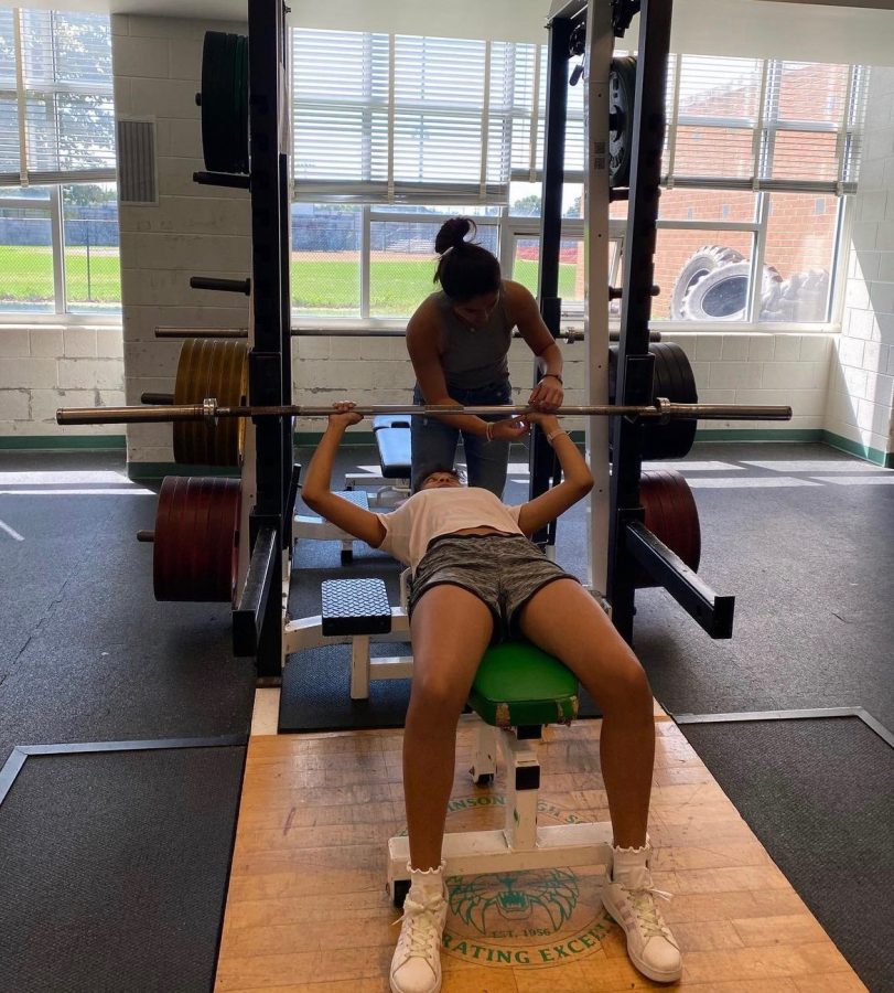 Senior club president Sophia Ikeda helps junior Ciella Koe Bi with a lift during a club workout. WJs Buff Cats clubs goal is to encourage girls of all weight lifting experience levels to join.