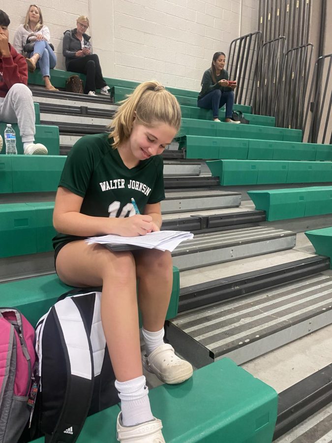 Freshman Annabelle Kehoe finds time after the JV volleyball game to do her homework while watching the varsity volleyball game. Its all about balancing sports and school, so I just have to find time to do my homework after the game, Kehoe said.