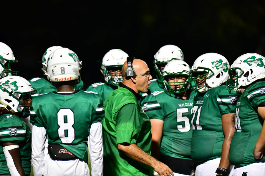 Larry Hurd Jr. in the middle of a huddle. As head football coach, Hurd Jr. elevated the football program to play against the highest level of public school football.