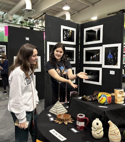 Senior Julia Schneider describes her work to a visitor. This exhibit features artwork from several different artists with both functional and decorative ceramics. 