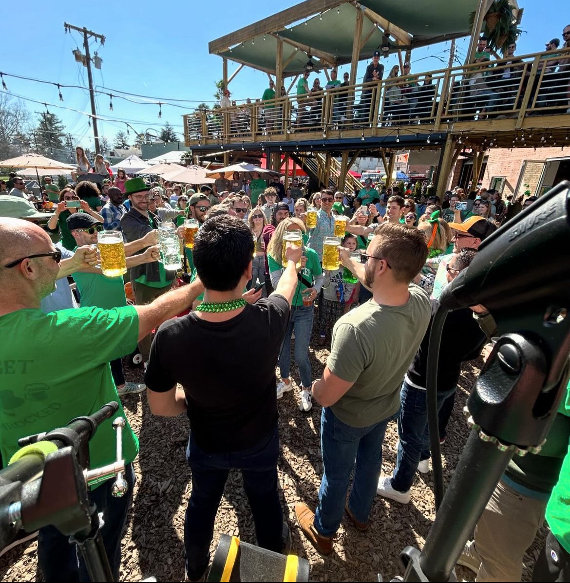 A group of adults stands in a circle at BabyCat’s outdoor area, raising their steins of beer in celebration.